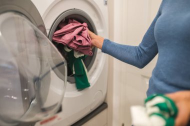 Çamaşır yıkama. Çamaşır makinesine çamaşır koyan kadın.