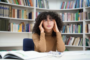 Esmer kadın mimar, dolu bir kütüphanenin planlarıyla çalışıyor.