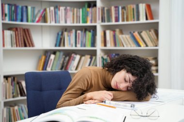 Kütüphanede planlarla çalışan yorgun kadın mimar ve masa başında uyuyakalıyor.