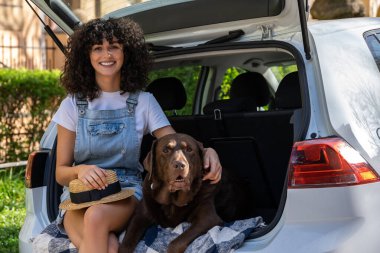 Birlikte mutluyuz. Şirin kıvırcık saçlı genç bir kadın arabada köpeğiyle oturuyor ve mutlu görünüyor.