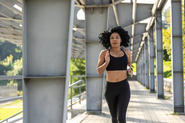 stock image Runner. Curly-haired woman in black sportswear running and looking focused