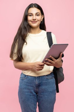 Sırt çantalı ve dijital tabletli gülümseyen genç kız pembe arka planda izole edilmiş.