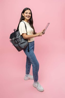 Sırt çantalı, dijital tabletli, pembe arka planda izole edilmiş online kolaj görevleri yapan mutlu genç kız öğrencilerle dolu.