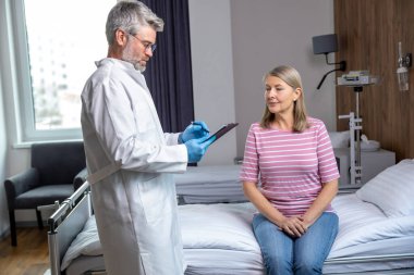 Hastanedeydim. Gri saçlı erkek doktor hastasını muayene ediyor.