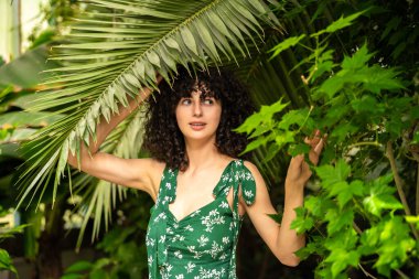 Yeşil yaprakların arasında siyah bukleleri olan egzotik bir kadın model.