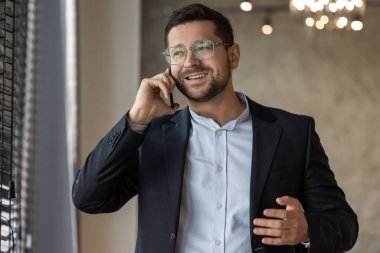 Resmi kıyafet giyen yakışıklı iş adamı cep telefonuyla içeride konuşuyor.