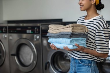 Kamu çamaşırhanesinde elinde birkaç katlanmış havlu tutan tanınmayan bir kadın.