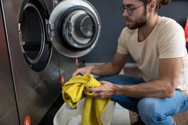 Beyaz sakallı kadın ev işlerini hallediyor çamaşırhanede çamaşır yıkıyor.