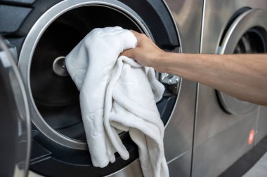 Çamaşırhanedeki kirli çamaşırlarla ilgilenen anonim bir adam çamaşır makinesine çamaşır koyuyor.