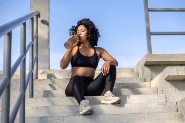 Susadım. Antrenmandan sonra merdivenlerde oturmuş su içen bayan sporcu.