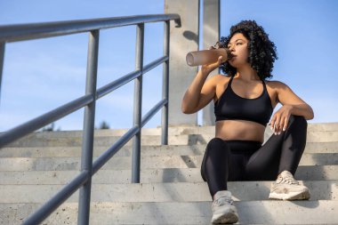 Susadım. Antrenmandan sonra merdivenlerde oturmuş su içen bayan sporcu.