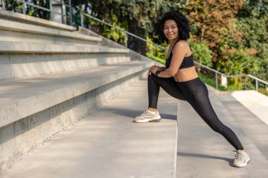 Açık havada idman. Esmer kadın gülümsüyor ve merdivenlerde hamleler yapıyor.