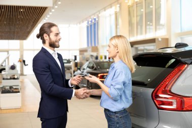 Modern galeride erkek satış asistanı yeni otomobilden kadın müşteriye anahtar veriyor.
