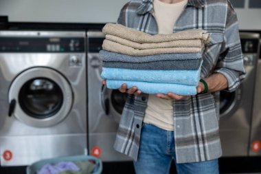 Endüstriyel çamaşırhanede katlanmış havluları olan tanınmayan isimsiz bir erkek.