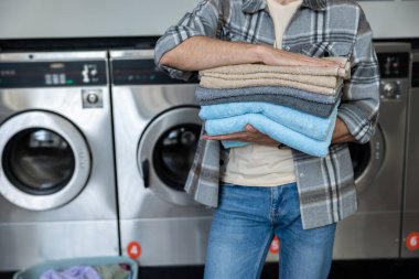 Kamu çamaşırhanesinde elinde birkaç katlanmış havlu tutan tanınmamış bir erkek.