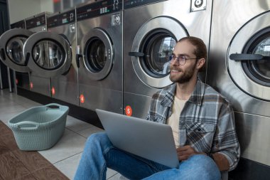 Sakallı adam uzaktan kumanda için teknolojiyi kullanıyor. Çamaşırhanenin çamaşırhanesinde bekliyor.