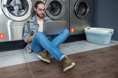 Sakallı adam uzaktan kumanda için teknolojiyi kullanıyor. Çamaşırhanenin çamaşırhanesinde bekliyor.