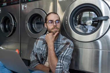 Düşünceli Kafkasyalı adam, umumi çamaşır merkezinde dizüstü bilgisayarla online işlerini bitiriyor.