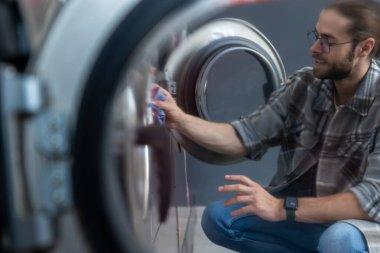 Çok çalışan beyaz sakallı adam çamaşırhanede çamaşır yıkıyor.