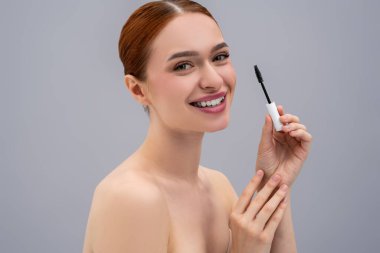 Kırbaç uzantısı olarak kozmetik fırça kullanan çekici bir kadın. Gri arka planda izole edilmiş.