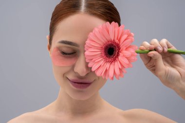 Gerbera çiçeği tutan ve kaldırma bantları kullanan kadın gri arka planda izole edilmiş kaplıca tedavisinin keyfini çıkarıyor.