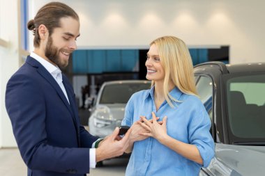 Beyaz kadın otomobil galerisindeki erkek iş danışmanının yardımıyla yeni araba seçiyor.