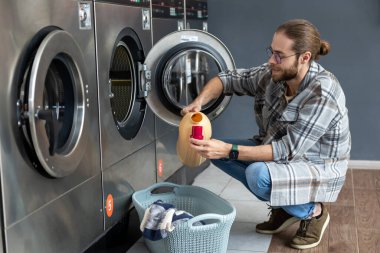 Çamaşırhanede otomatik çamaşır makinesi kullanan ev hanımı sakallı bir erkek.