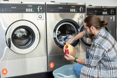 Beyaz sakallı yetişkin bir adam kamu çamaşırhanesinde çamaşırhane yönetiyor.