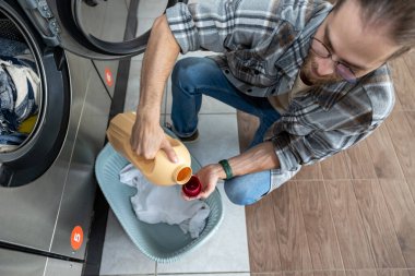 Beyaz sakallı adam çamaşırhanede çamaşır yıkıyor.