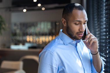 Pencerenin yanındaki genç siyahi adam kafenin içinde akıllı telefondan konuşuyor.