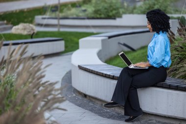 Çalışıyorum. Laptoplu esmer kadın bankta oturuyor ve çalışıyor.