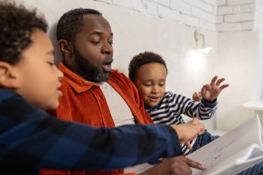 Uyku zamanı hikayeleri. Baba ve çocuklar uyumadan önce masal okuyor ve ilgileniyorlar.