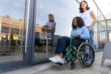 Arkadaşız. Engelli bir Afrikalı Amerikalı kadınla tekerlekli sandalye taşıyan genç bir kadın.