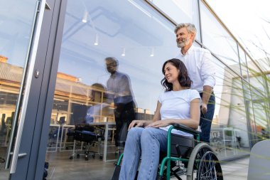 Şefkatli adam. Adam karısının tekerlekli sandalyesini taşıyor ve ona sevgiyle bakıyor.