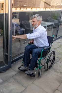 Engelli. Ofis bölgesinde tekerlekli sandalyede oturan gri saçlı, olgun bir adam.