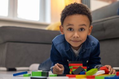 Mutlu Afro-Amerikan çocuk, evdeki tuğlalardan ve bloklardan kulede oturuyor.