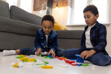 Tatlı erkek arkadaşlar yerde oturup renkli inşaatçılarla oynuyorlar.