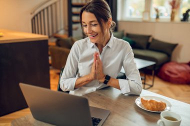 Görüntülü arama. Koyu renk saçlı güzel bir kadın dizüstü bilgisayarda oturuyor ve video görüşmesi yapıyor.