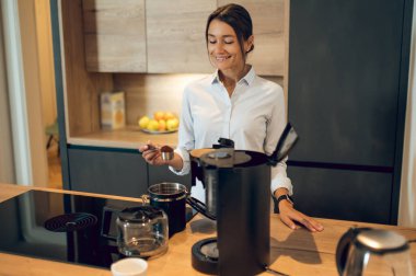 Kahve yapıyorum. Koyu saçlı genç bayan mutfakta kahve makinesinde kahve yapıyor.