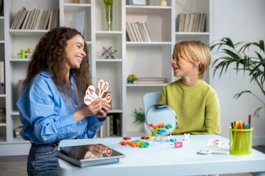 Konuşma egzersizleri. Uzun saçlı konuşma terapisti sarışın bir çocuğa egzersiz yapıyor.