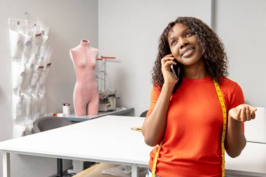 Afrika kökenli Amerikalı kadın terzi müşteri yönetimi ve müşteri siparişleri ile akıllı telefondan konuşuyor.