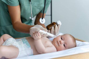 Gülümseyen doktor klinikteki hasta bebeğe şurup veriyor.