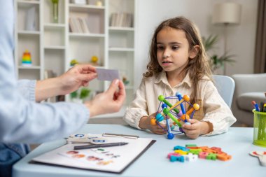 Konuşma terapisi. Tatlı bir kız konuşma terapistiyle eğitim seansı yapıyor ve ilgili görünüyor.