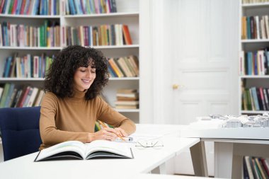 Eğitim. Kütüphanedeki masada oturan tatlı kıvırcık saçlı kadın.