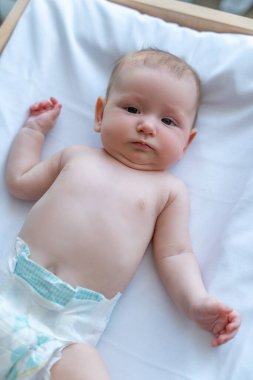 Bebek ya da çocuk bezi takmış, masanın üstünde uzanmış kameraya bakıyor.