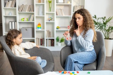 Konuşma egzersizleri. Uzun saçlı kadın konuşma terapisti küçük bir kıza egzersiz gösteriyor.