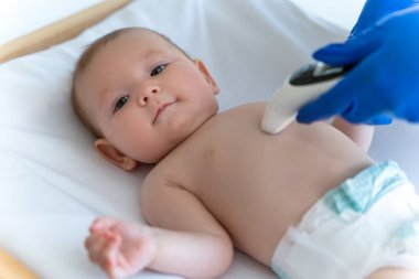 Mavi eldivenli doktor ya da hemşire bebek sıcaklığını dijital termometreyle izliyor.