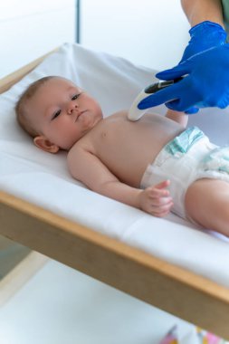 Mavi eldivenli doktor ya da hemşire bebek sıcaklığını dijital termometreyle izliyor.