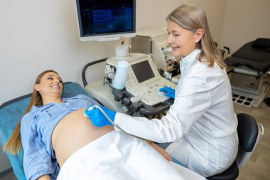 Ultrasonografi. Uzun saçlı, olgun bir doktor hamile bir kadına ultrasonografi yapıyor.
