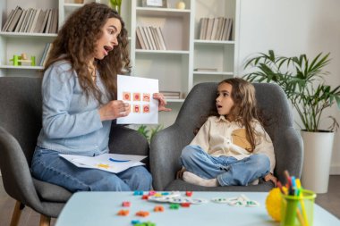 Eğitim seansı. Uzun saçlı tatlı bir kız konuşma terapistiyle çalışıyor ve özenli görünüyor.